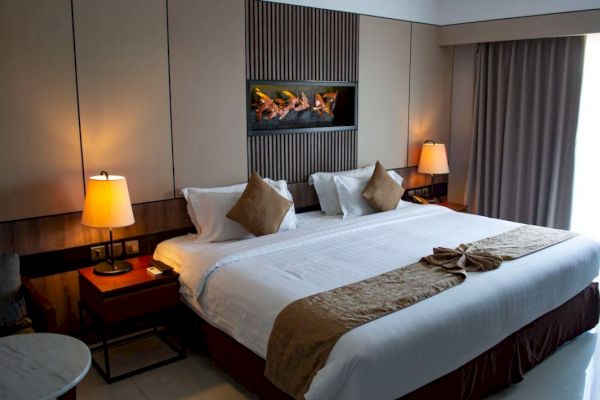A neatly decorated hotel room features a large bed with pillows and lamps on either side, along with a modern wall decoration above.