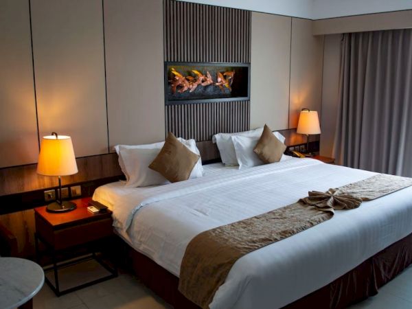 A neatly decorated hotel room features a large bed with pillows and lamps on either side, along with a modern wall decoration above.