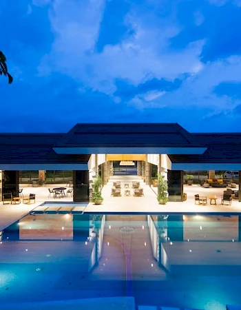 Luxurious poolside with a modern building in the background, illuminated against a twilight sky, creating a serene and inviting atmosphere.