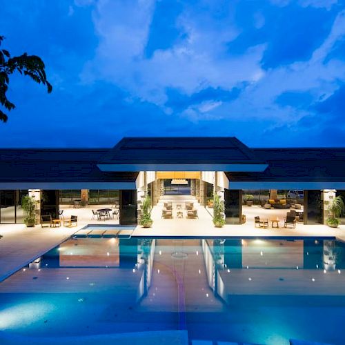 A luxurious house with a large illuminated pool under a vibrant evening sky.