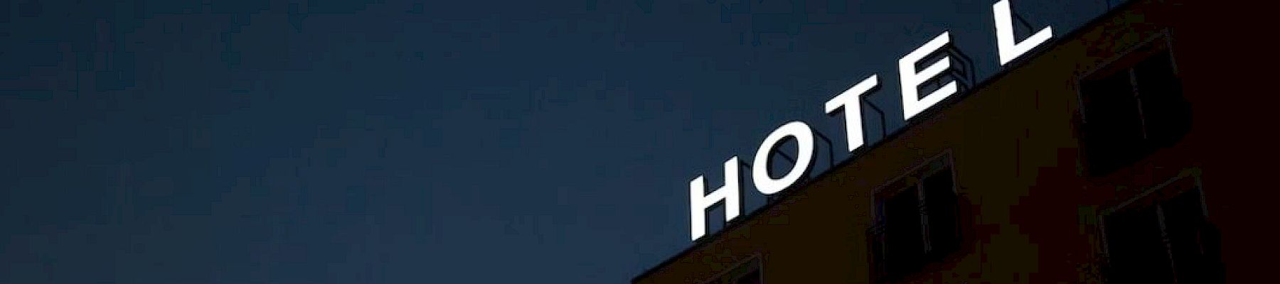 The image shows a building with the illuminated word "HOTEL" on the roof at night, with an "E" missing.
