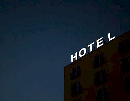 The image shows a building with the illuminated word "HOTEL" on the roof at night, with an "E" missing.
