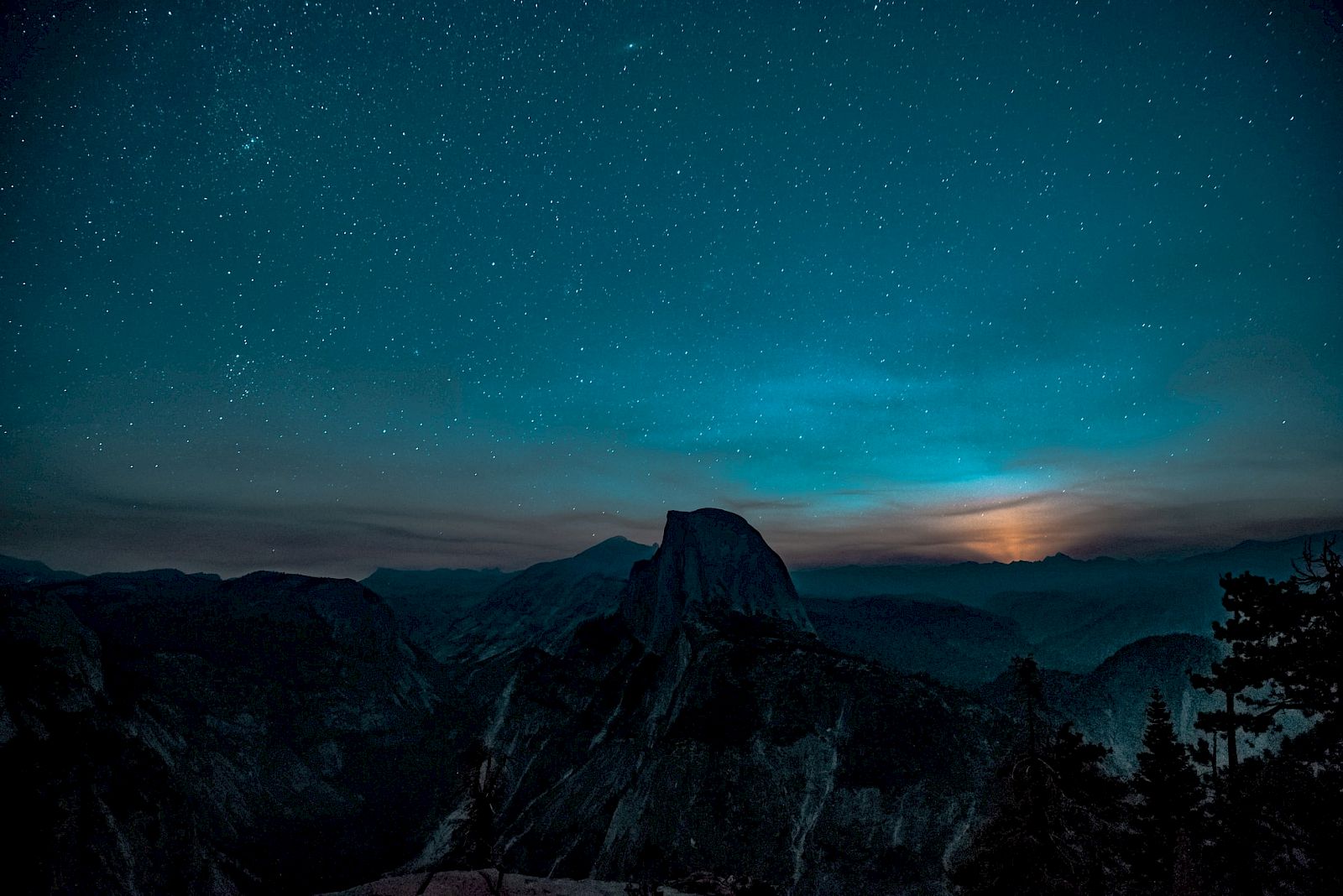 A starry night sky over a mountain silhouette with scattered clouds and a faint horizon glow creating a serene, mystical atmosphere.