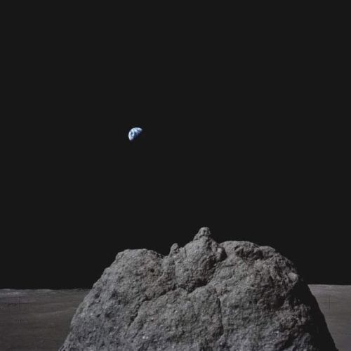 A rocky lunar surface with Earth visible in the distant, dark sky.