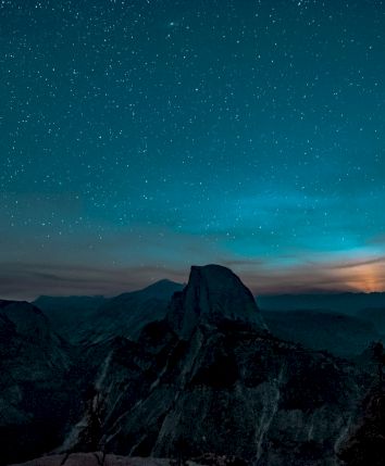 Starry night sky over a mountain landscape with a glowing horizon, creating a serene and otherworldly atmosphere.