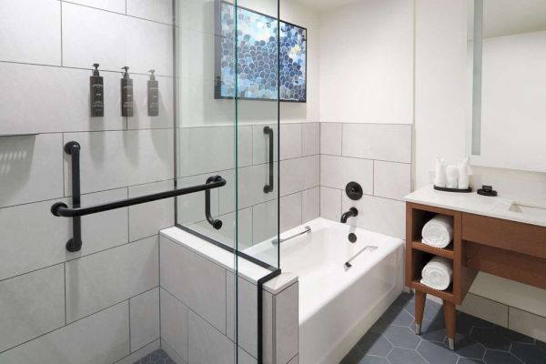 A modern bathroom with a glass-enclosed shower, a tub, a sink with a wooden cabinet, and a hexagonal tile floor.