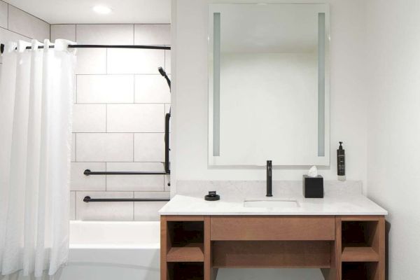 The image shows a modern bathroom with a bathtub, white shower curtain, vanity with mirror, sink, and wooden shelves, all in a minimal design.