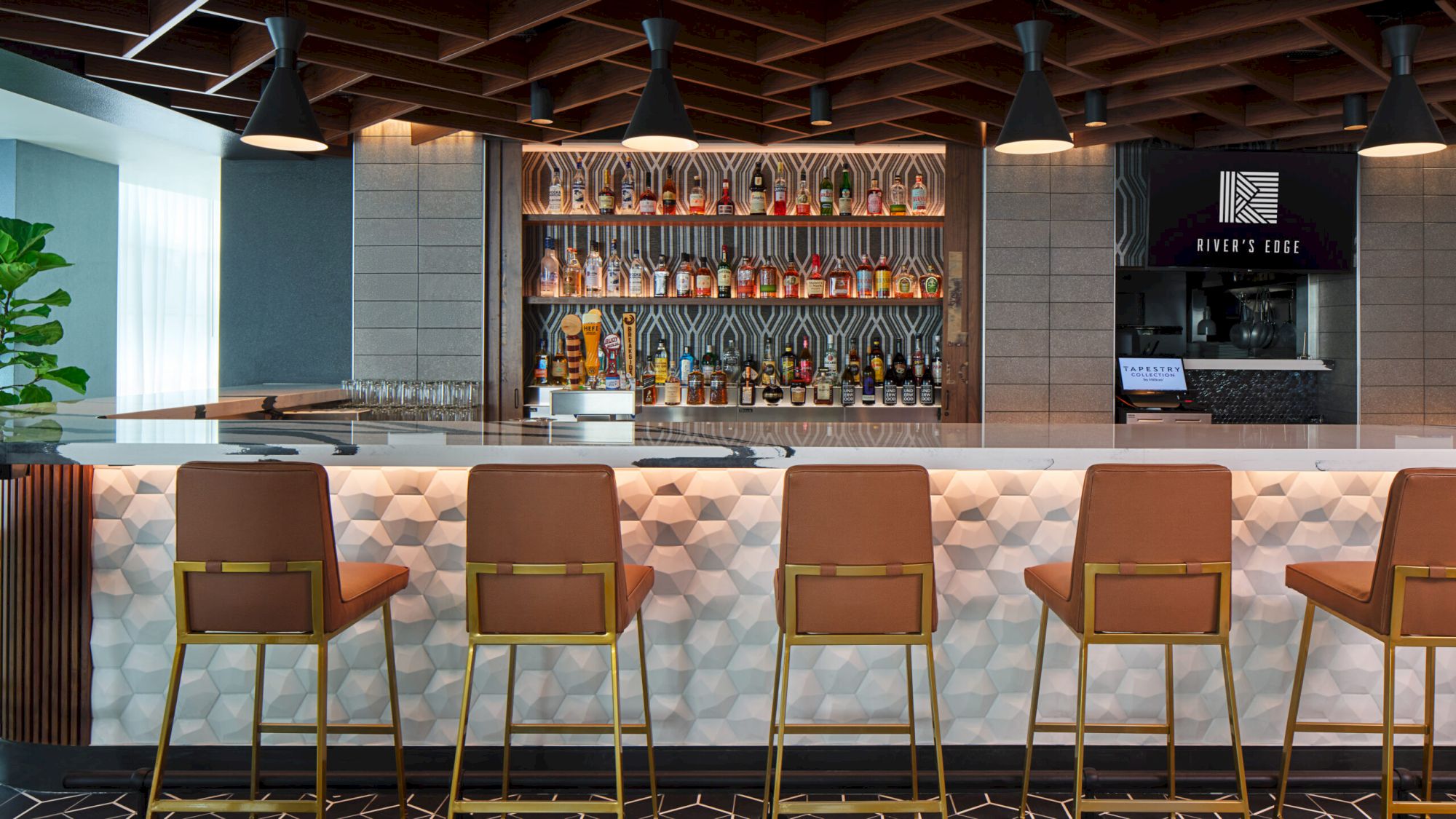 A stylish bar with a modern design features high stools, a well-stocked shelf, and geometric patterns on the counter, creating a chic atmosphere.