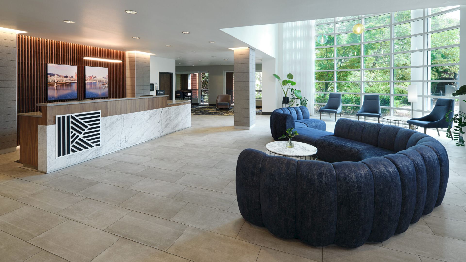 A modern lobby featuring a reception desk, blue velvet sofa, and large windows letting in natural light.