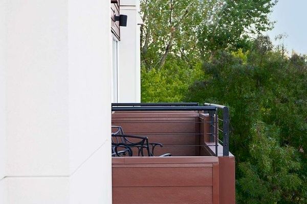 The image shows a row of balconies on a building with trees in the background and clear skies above.