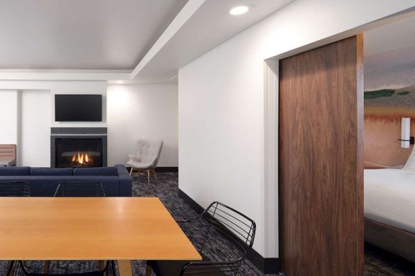 The image shows a modern living space with a fireplace, TV, sofa, dining table, and a glimpse of a bedroom through a sliding door.