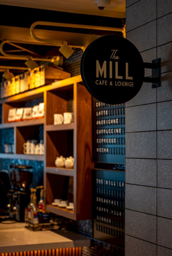 A cozy cafe storefront with warm lights, shelves of teapots and cups, and a round sign reading “The Mill Café & Lounge.”