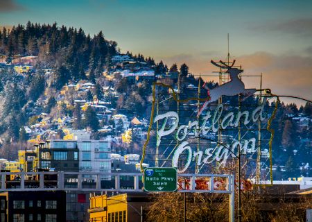 A famous Portland, Oregon sign with a leaping deer is in the foreground, with a wooded hill and buildings in the background.
