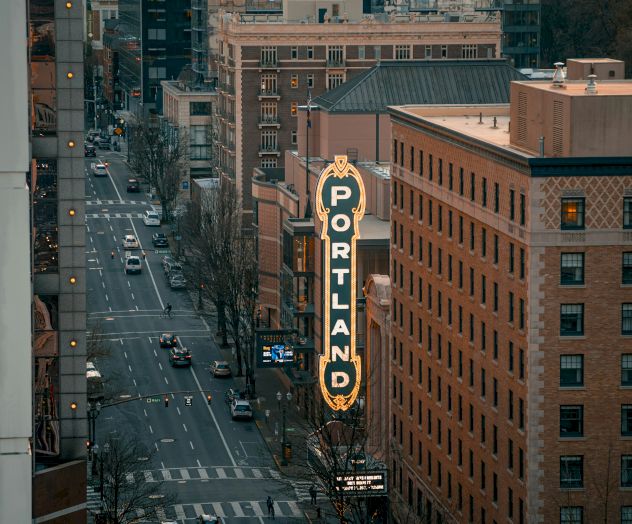 An urban scene with a street lined by buildings and a "Portland" sign prominently displayed on one of them.