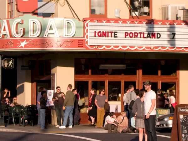 People are gathered outside the Bagdad Theater, which has a marquee that reads "Ignite Portland 7," indicating an event.