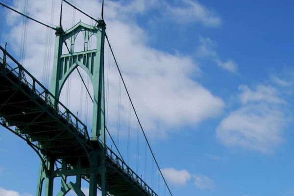 The image shows a green suspension bridge structure against a blue sky with some clouds.