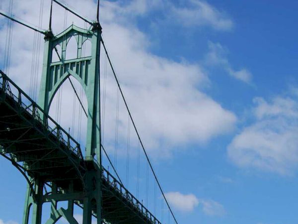 The image shows a green suspension bridge structure against a blue sky with some clouds.
