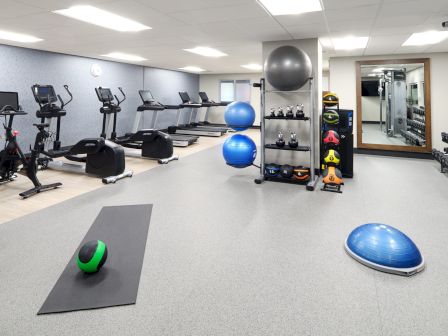 A gym room with exercise bikes, treadmills, yoga mats, medicine balls, and other equipment neatly arranged.