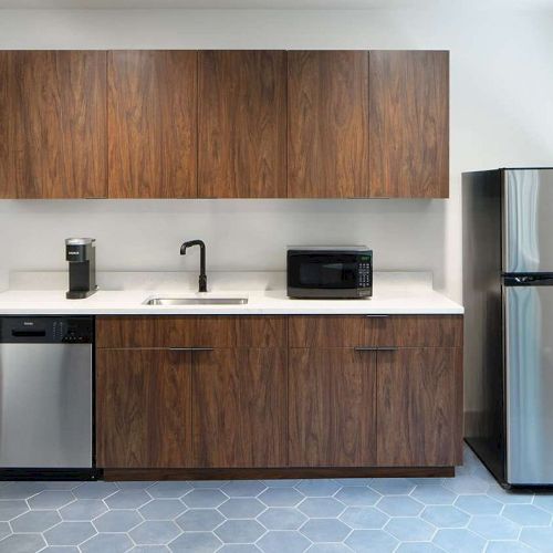 A modern kitchen with a fridge, microwave, coffee maker, dishwasher, sink, wooden cabinets, and a window with a view.