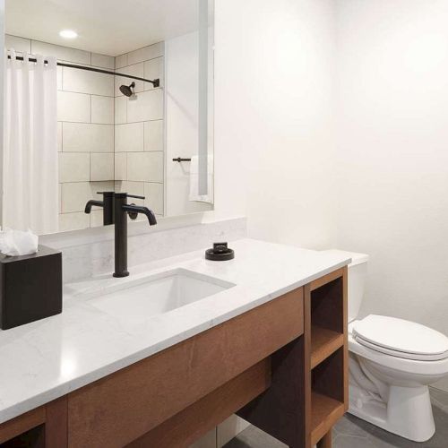 A clean, modern bathroom with a shower, sink, mirror, toilet, and toiletries on the countertop, all in a minimalist design.