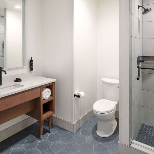 A modern bathroom with a large mirror, sink, toilet, and shower featuring white tiles and hexagonal floor tiles.