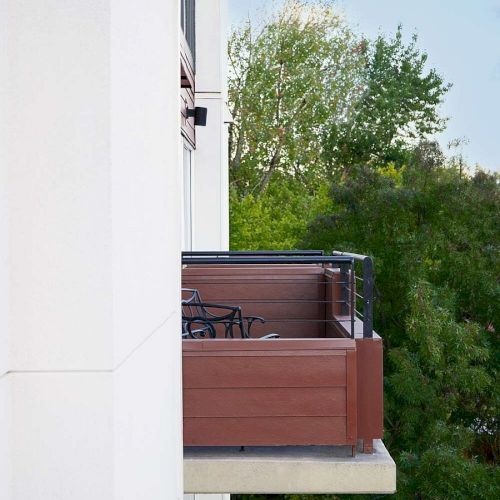 The image shows balconies with chairs attached to a white building, surrounded by green trees and a clear blue sky.