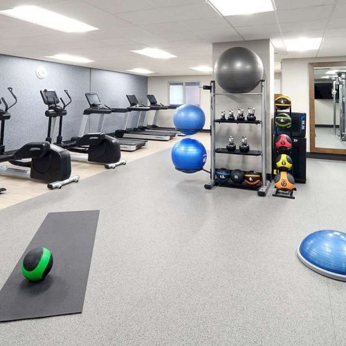 A gym room with exercise bikes, treadmills, weights, a yoga mat, fitness balls, kettlebells, and a wall mirror.