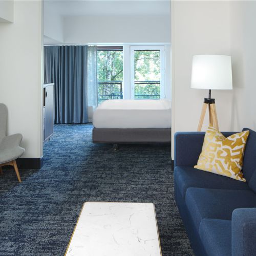 A modern living space with a fireplace, sofa, armchair, and a bed in the adjoining room.