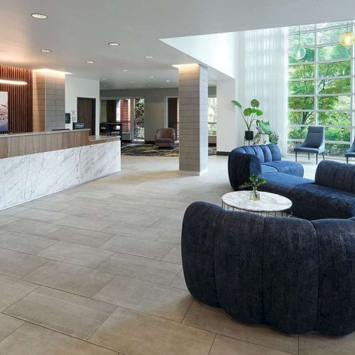 The image shows a modern hotel lobby with a reception desk, cozy seating, large windows, and stylish decor.