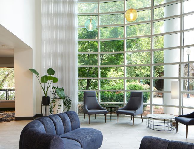 A modern lounge with a curved blue sofa, large windows, hanging lights, and plants, creating a serene atmosphere with natural light.