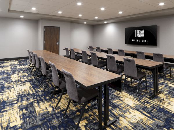 A conference room with long tables, chairs, a patterned carpet, and a wall-mounted screen displaying "MEET & STAY".