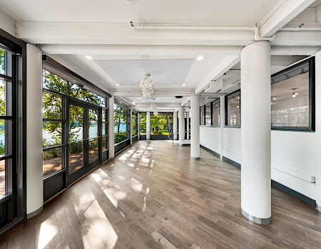 Bright modern hallway with floor-to-ceiling windows, white columns, wood floors, and hanging pendant lights.