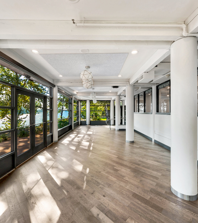 Bright modern hallway with floor-to-ceiling windows, white columns, wood floors, and hanging pendant lights.