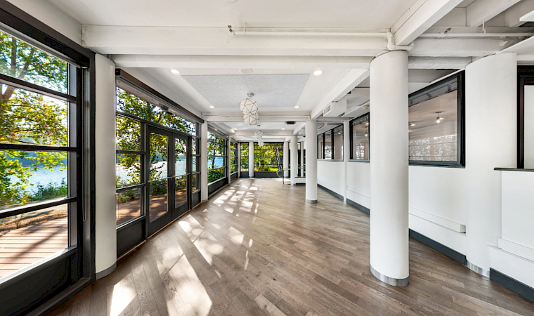 Bright modern hallway with floor-to-ceiling windows, white columns, wood floors, and hanging pendant lights.