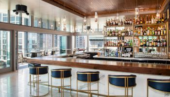 Luxurious bar interior with chic seating, well-lit with large windows and a wide selection of spirits on the shelves.