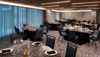 A decorated banquet hall with round tables set with glassware, plates, and napkins, ready for an event.