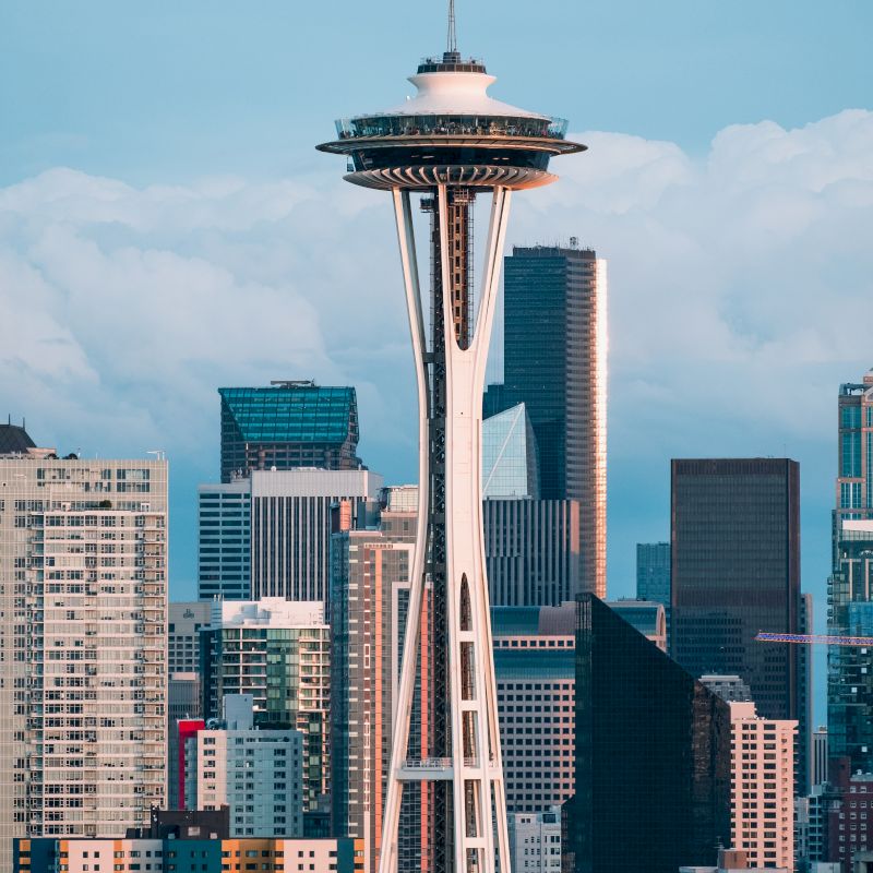 A cityscape featuring a prominent observation tower, surrounded by various skyscrapers under a partly cloudy sky.