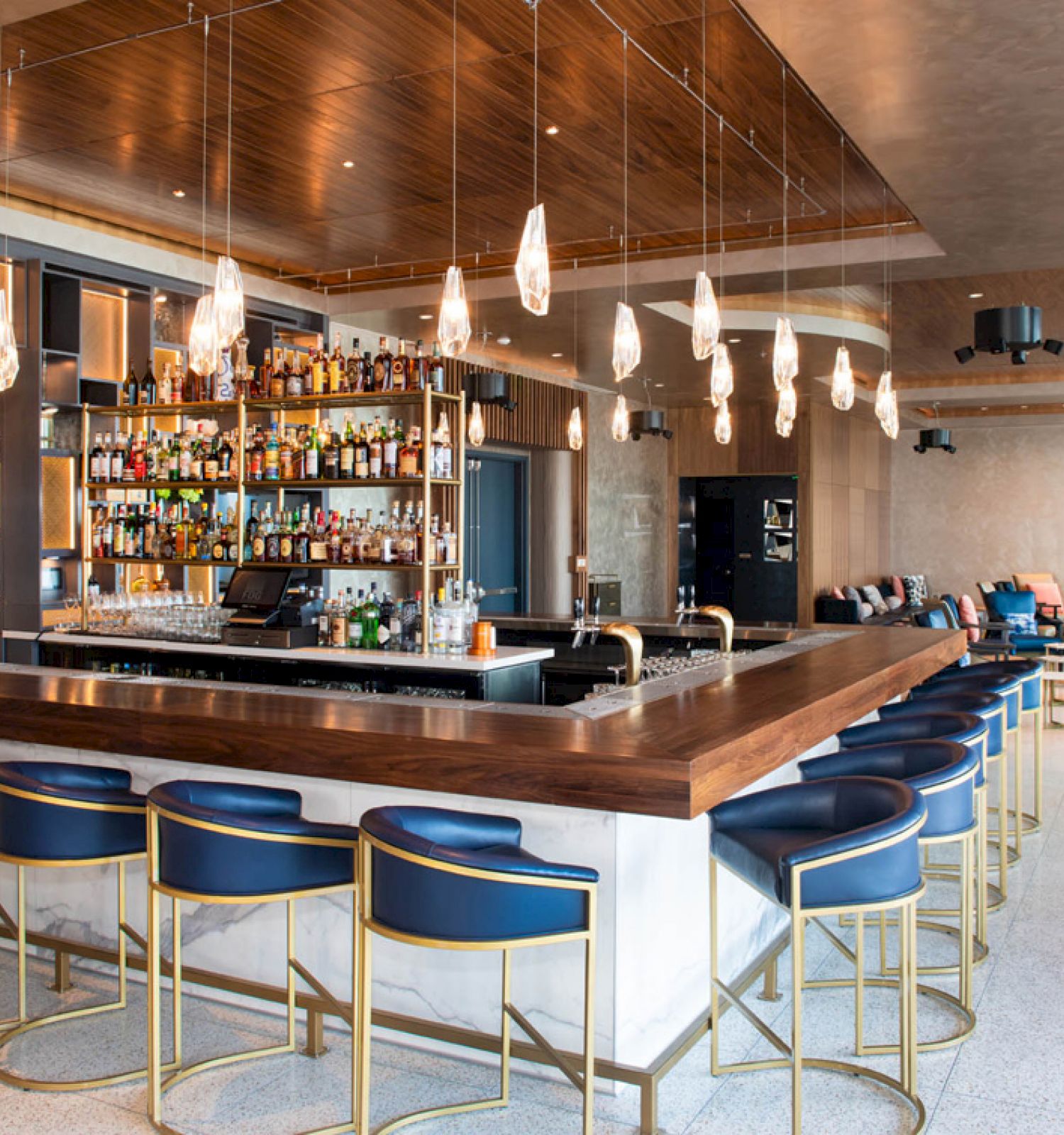 A modern bar with blue barstools, hanging lights, and a well-stocked bar counter in an elegant lounge setting.